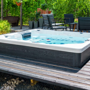 Large hot tub embedded in the backyard terrace. A sunny summer's day in the shelter of a green garden. Everyday luxury and relaxation in your own backyard. Spa complex, vacation and traveling concept.